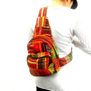 Op de afbeelding: Een rood, groen, geel en blauw gepatroneerde schoudertas met een lange band. De tas heeft een klep sluiting en een ritsvak aan de voorkant.