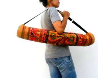 May include: A colorful yoga mat bag with a black strap. The bag is made of fabric with a floral pattern in shades of orange, yellow, green, and red.