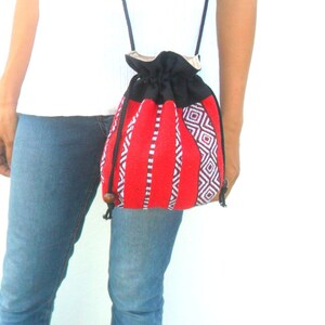May include: A red and black drawstring bag with a geometric pattern. The bag has a long strap and is worn over the shoulder.