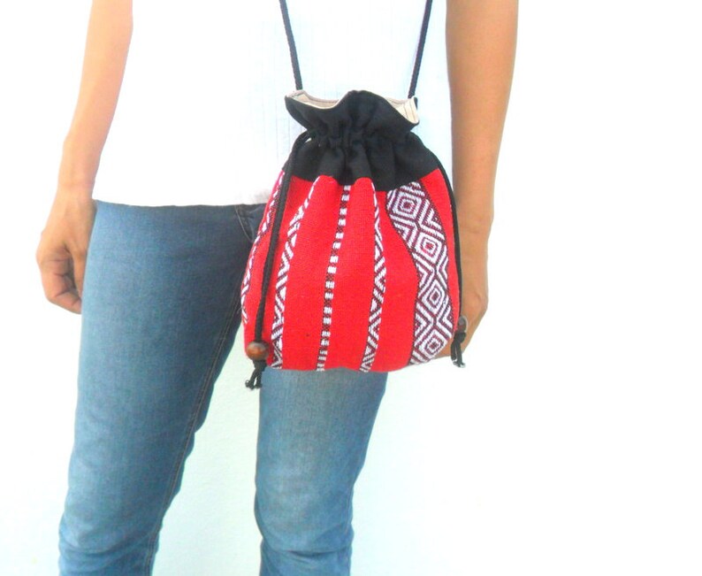 May include: A red and black drawstring bag with a geometric pattern. The bag has a long strap and is worn over the shoulder.