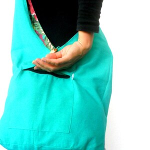 May include: A turquoise blue tote bag with a smaller pocket on the front. The bag is made of a soft, fabric material.