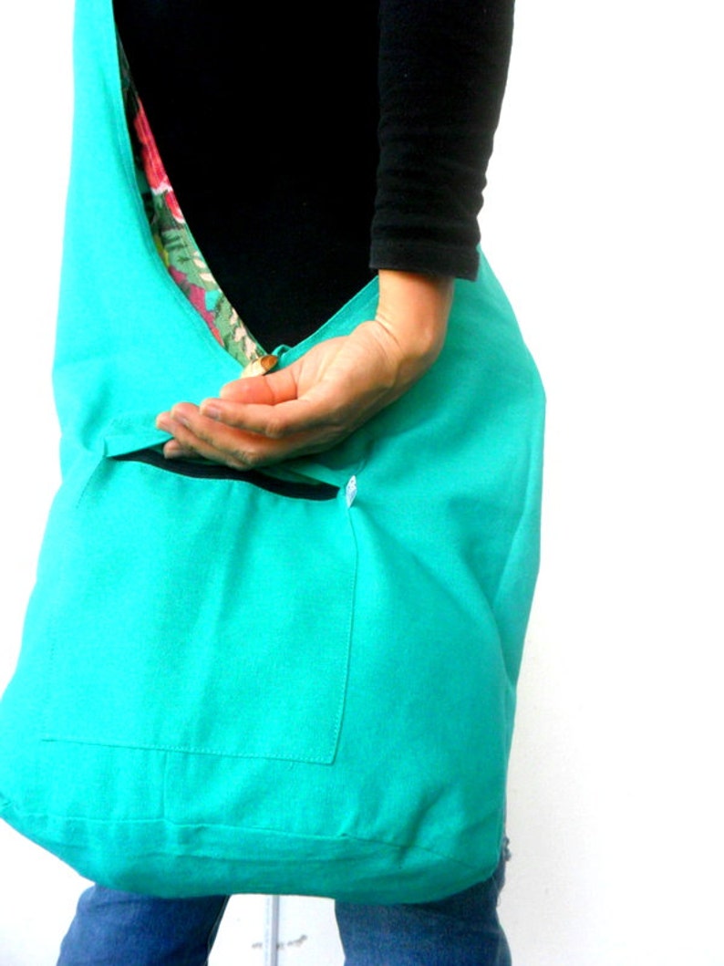 May include: A turquoise blue tote bag with a smaller pocket on the front. The bag is made of a soft, fabric material.