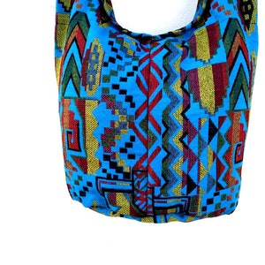 May include: A blue and multi-colored tote bag with a geometric pattern. The bag has a long strap and is made of a woven fabric.