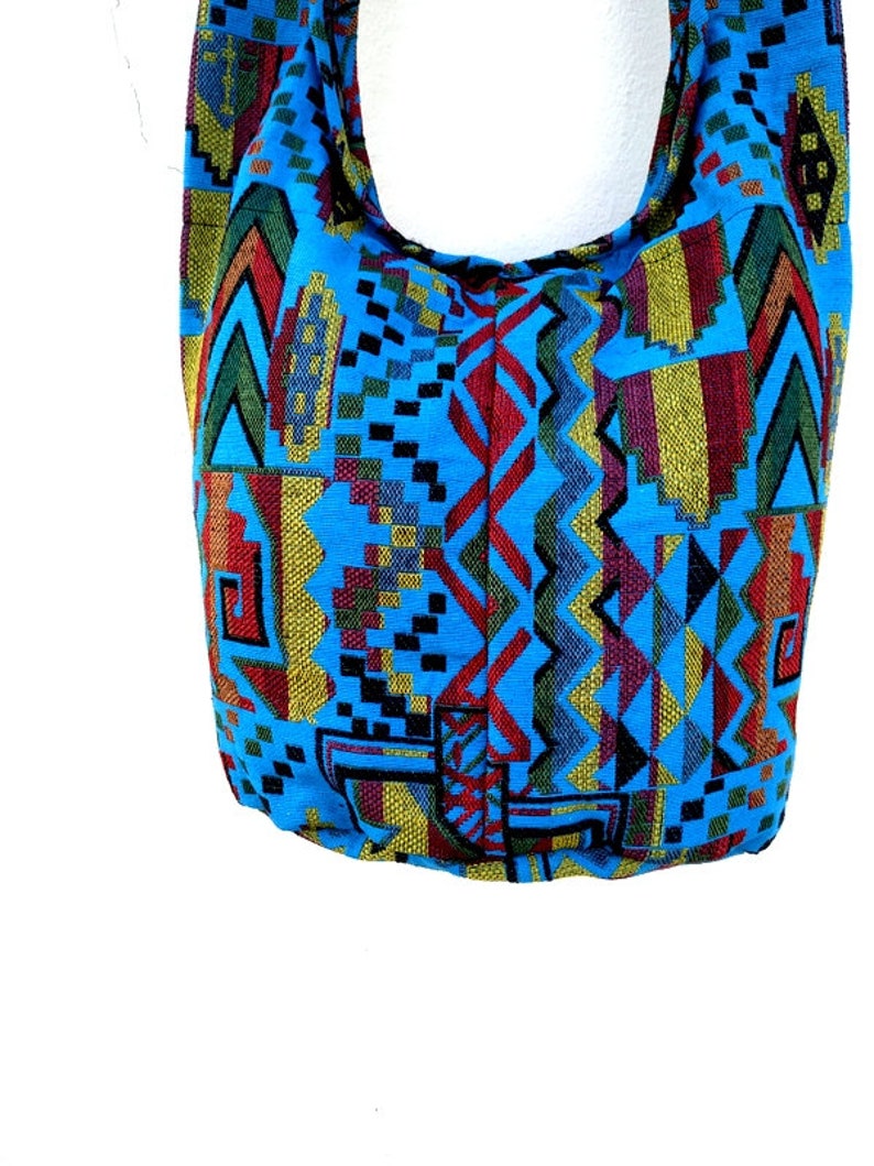 May include: A blue and multi-colored tote bag with a geometric pattern. The bag has a long strap and is made of a woven fabric.