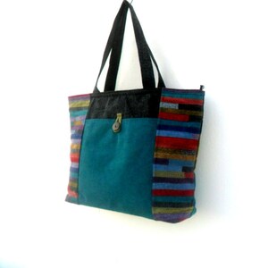 May include: A teal blue tote bag with a black handle and a colourful striped panel on the side. The bag has a flap with a button closure.