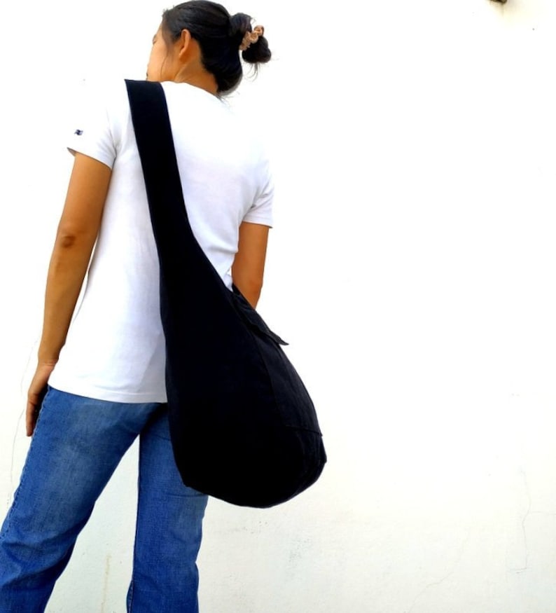 Pode incluir: Uma pessoa vestindo jeans azul e uma camiseta branca est&aacute; carregando uma grande bolsa tote preta no ombro.
