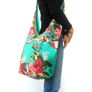 May include: A large turquoise floral print tote bag with a long strap. The bag has a pocket on the front and is made of a soft, fabric material.
