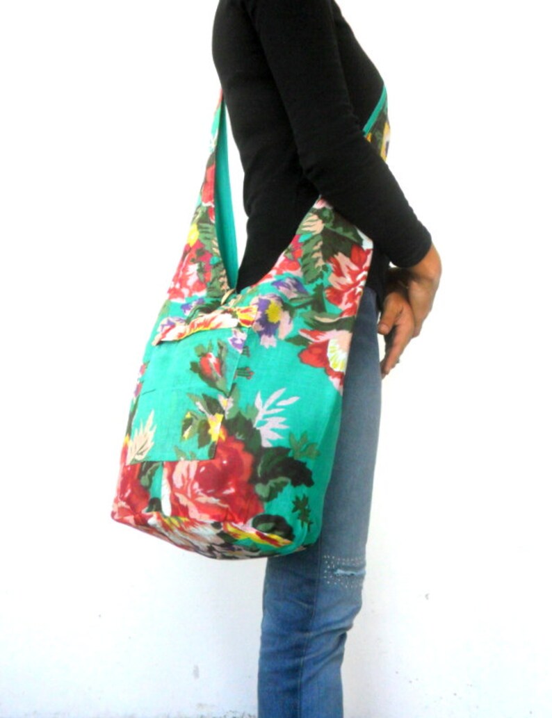 May include: A large turquoise floral print tote bag with a long strap. The bag has a pocket on the front and is made of a soft, fabric material.