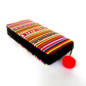 Puede incluir: Una cartera de rayas coloridas con una cremallera negra y un pomp&oacute;n rojo.