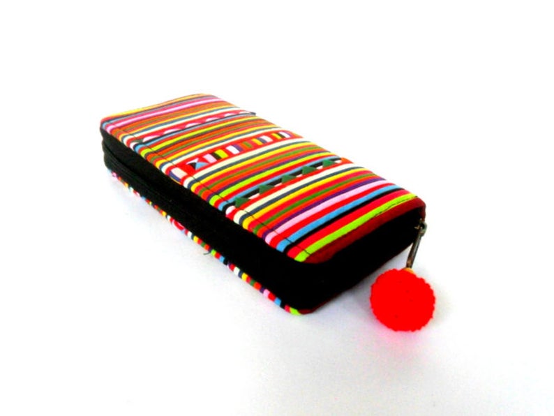 Puede incluir: Una cartera de rayas coloridas con una cremallera negra y un pomp&oacute;n rojo.