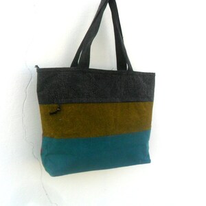 May include: A striped tote bag with a grey, brown, and teal colour scheme. The bag has a zipper closure and two handles.