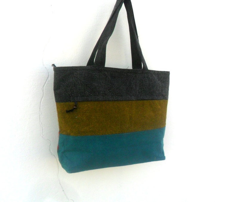 May include: A striped tote bag with a grey, brown, and teal colour scheme. The bag has a zipper closure and two handles.