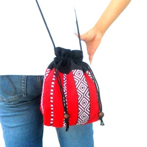 May include: A red and black drawstring bag with a geometric pattern. The bag has a long black strap and is worn over the shoulder.