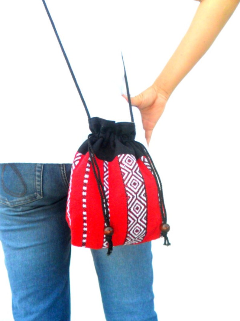 May include: A red and black drawstring bag with a geometric pattern. The bag has a long black strap and is worn over the shoulder.