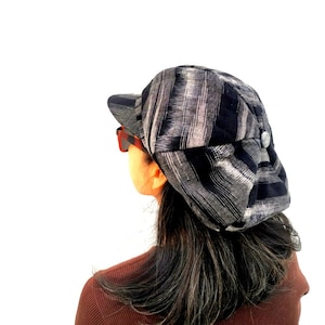 Puede incluir: Una persona con una gorra de estilo newsboy a rayas blancas y negras con un botón en el lateral.