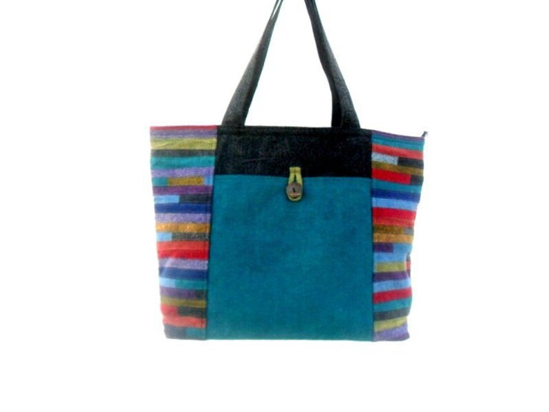 May include: A teal blue tote bag with black straps and colourful striped fabric on the sides. The bag has a flap with a wooden button closure.