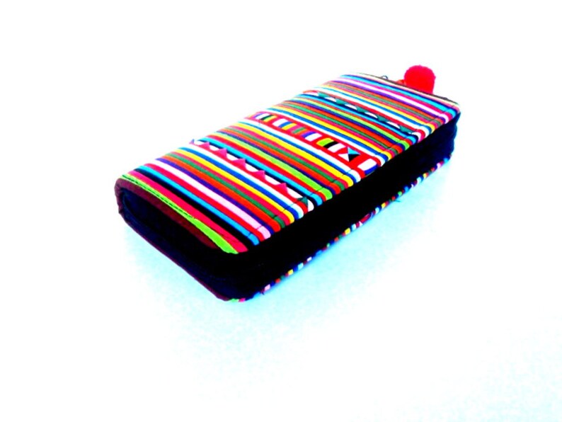 Puede incluir: Una cartera de rayas coloridas con una cremallera negra y un pomp&oacute;n rojo.