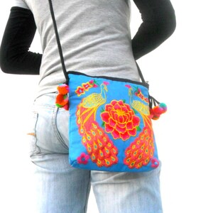 May include: A blue crossbody bag with embroidered peacocks and flowers. The bag has a long strap and a tassel.