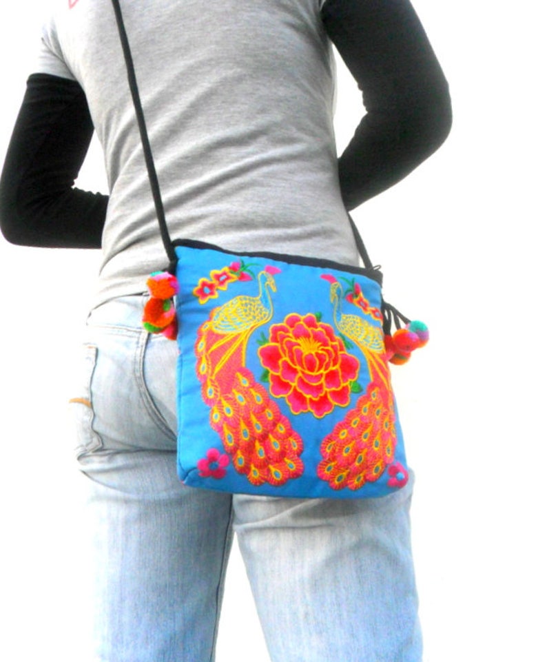May include: A blue crossbody bag with embroidered peacocks and flowers. The bag has a long strap and a tassel.