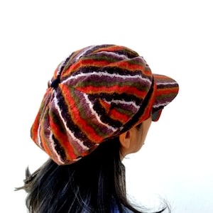 May include: A striped newsboy cap with a brown, orange, red, white, and green color scheme. The cap is made of a soft, textured fabric.