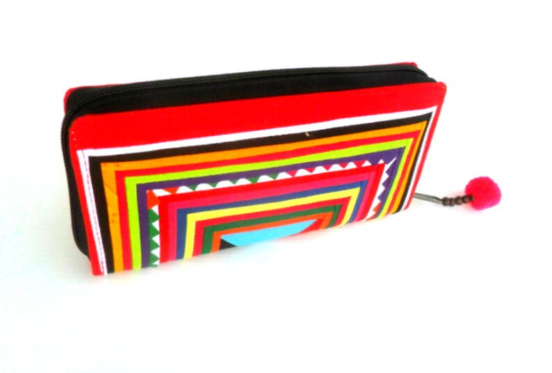 May include: A red zippered wallet with a colorful geometric pattern and a pink tassel.