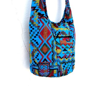 May include: A blue and multi-colored patterned hobo bag with a zippered pocket. The bag has a long strap for carrying over the shoulder.