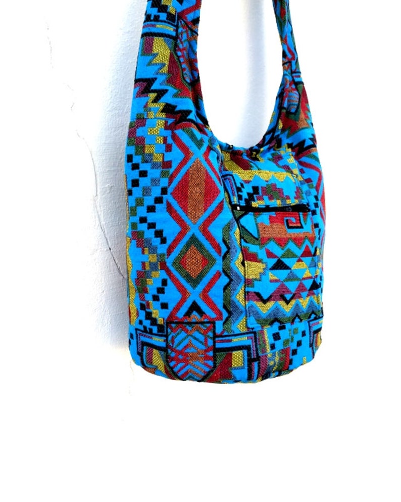 May include: A blue and multi-colored patterned hobo bag with a zippered pocket. The bag has a long strap for carrying over the shoulder.