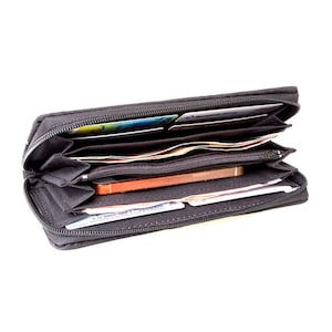 Puede incluir: Una cartera negra con cremallera con varios compartimentos, abierta para revelar efectivo, tarjetas y un tel&eacute;fono m&oacute;vil.