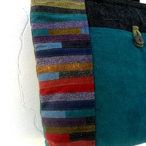 May include: A teal blue tote bag with a black fabric top and a colourful striped panel on the side. The bag has a single button closure.