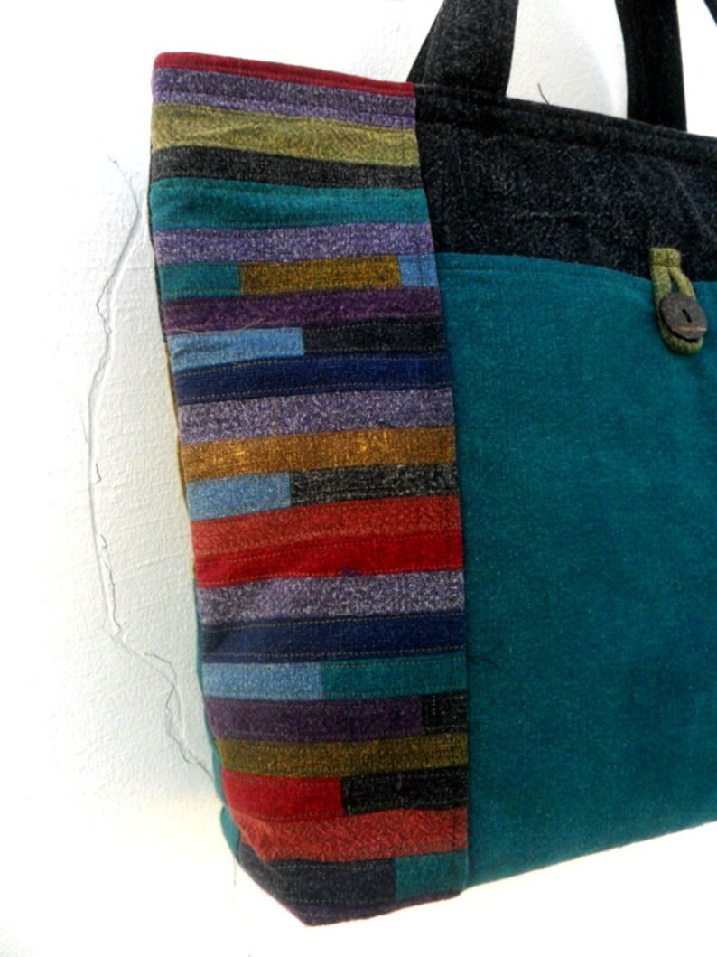 May include: A teal blue tote bag with a black fabric top and a colourful striped panel on the side. The bag has a single button closure.