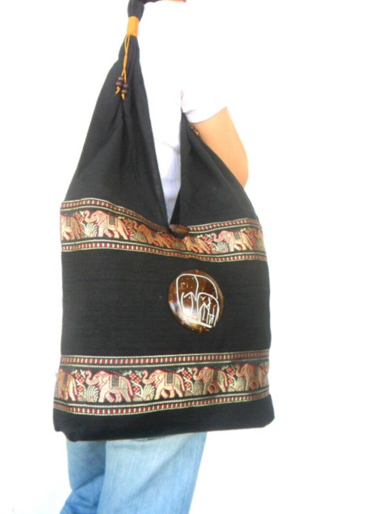 May include: Black cotton tote bag with a brown coconut shell elephant design. The bag has a gold and red trim with an elephant pattern.