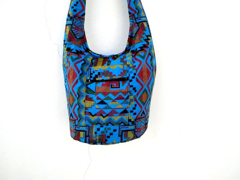 May include: A blue and red patterned shoulder bag with a zippered pocket. The bag is made of woven fabric and has a geometric design.