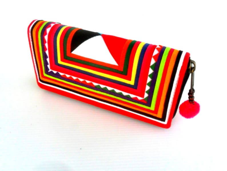 May include: A red, black, white, and multi-colored striped clutch purse with a pink tassel. The purse has a geometric design and is made of fabric.