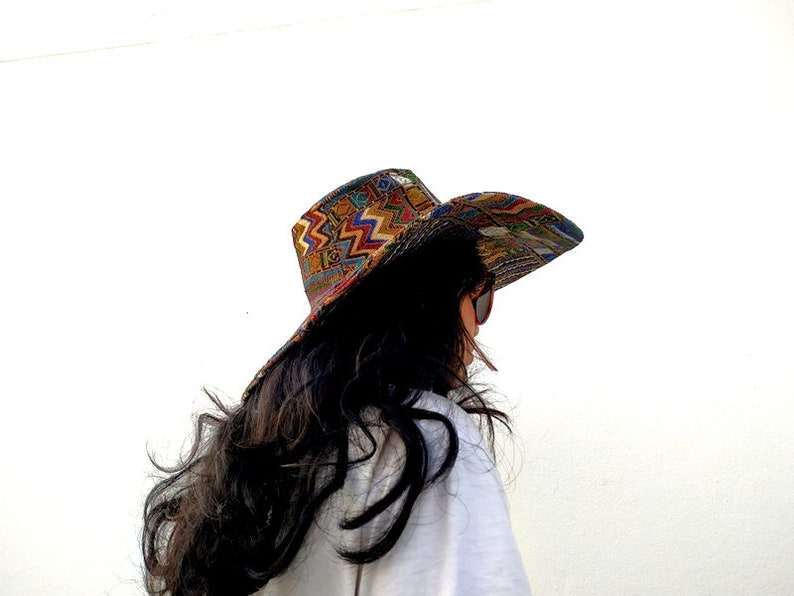 Puede incluir: Una mujer con el pelo largo y oscuro lleva un sombrero de ala ancha con un estampado geom&eacute;trico colorido. El sombrero est&aacute; hecho de tela y tiene un ala ligeramente curvada. La mujer est&aacute; de espaldas a la c&aacute;mara y mira hacia la derecha.