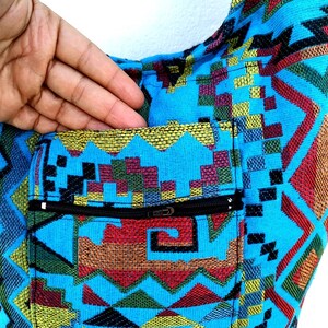 May include: A blue and multi-colored patterned tote bag with a zippered pocket. The bag has a geometric design with a variety of colors, including red, yellow, green, and black.