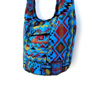 May include: A blue and red patterned shoulder bag with a zippered pocket. The bag is made of a woven fabric with geometric designs.