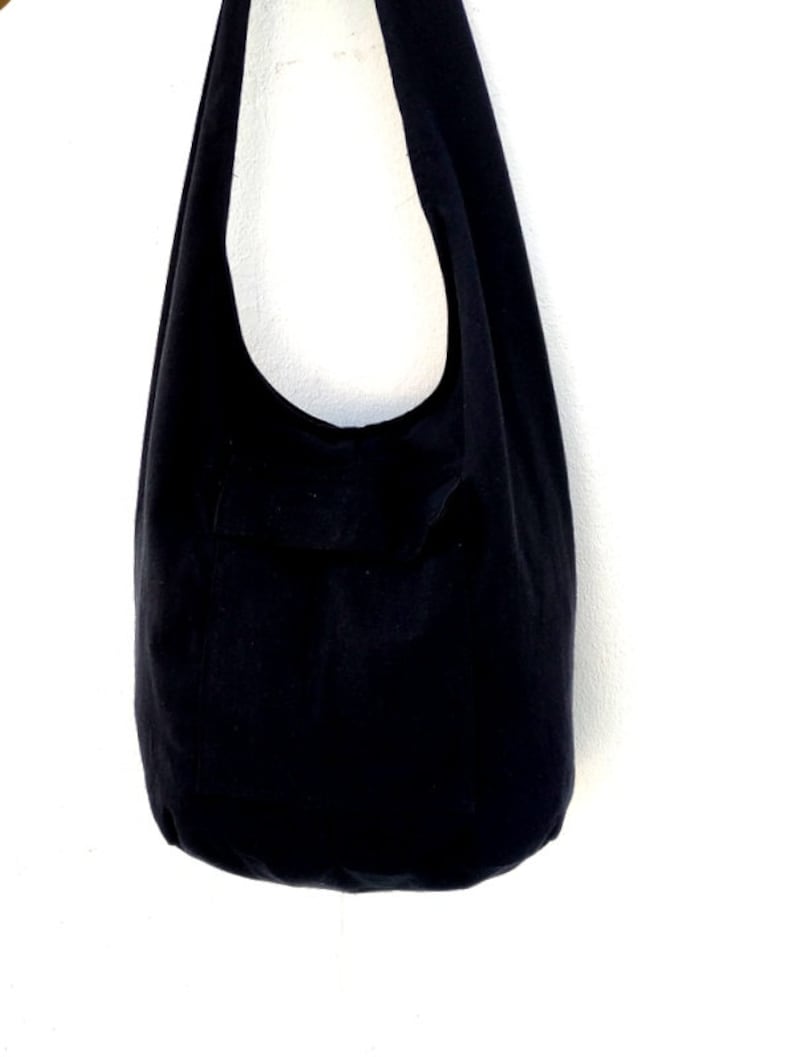 Pode incluir: Uma bolsa tote de lona preta com uma &uacute;nica al&ccedil;a. A bolsa est&aacute; pendurada em um gancho.