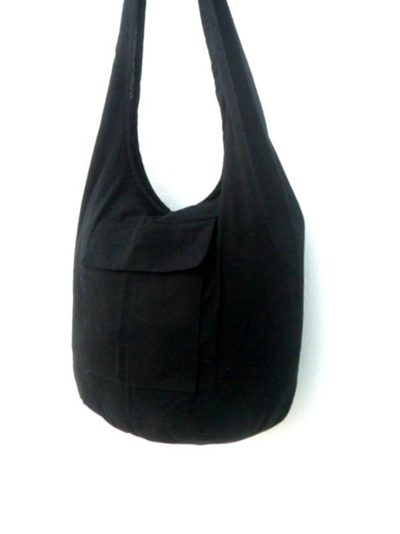 Pode incluir: Uma bolsa tote de lona preta com um bolso grande na frente. A bolsa tem uma al&ccedil;a longa para carregar no ombro.