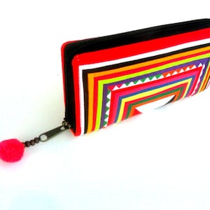 May include: A red zippered wallet with a colorful geometric pattern. The pattern is made up of stripes and triangles in shades of red, orange, yellow, green, blue, and purple.