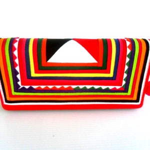 May include: A red fabric clutch with a colorful geometric pattern. The clutch has a zipper closure and a small tassel.