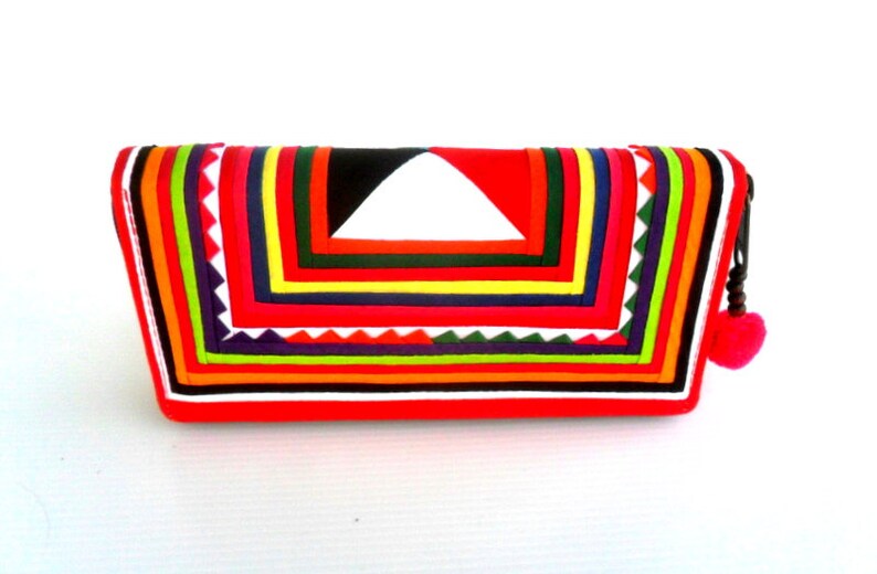 May include: A red fabric clutch with a colorful geometric pattern. The clutch has a zipper closure and a small tassel.