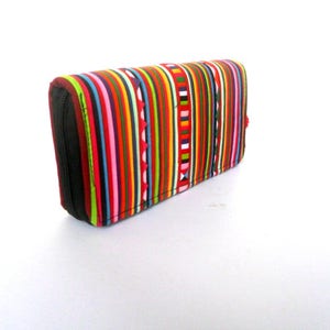 Puede incluir: Una cartera de rayas coloridas con cierre de cremallera. La cartera est&aacute; hecha de tela y tiene una variedad de colores, incluyendo rojo, verde, azul, amarillo y blanco.