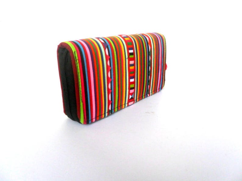 Puede incluir: Una cartera de rayas coloridas con cierre de cremallera. La cartera est&aacute; hecha de tela y tiene una variedad de colores, incluyendo rojo, verde, azul, amarillo y blanco.