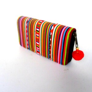 Puede incluir: Una cartera a rayas de colores con cierre de cremallera y un borla roja. La cartera est&aacute; hecha de tela y tiene una variedad de colores, incluyendo rojo, naranja, amarillo, verde, azul y morado.