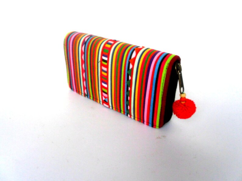 Puede incluir: Una cartera a rayas de colores con cierre de cremallera y un borla roja. La cartera est&aacute; hecha de tela y tiene una variedad de colores, incluyendo rojo, naranja, amarillo, verde, azul y morado.