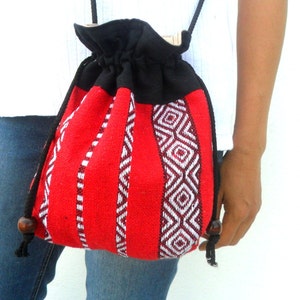 May include: A red and black drawstring bag with a geometric pattern. The bag is made of woven fabric and has a black drawstring closure. The bag is being worn by a person.