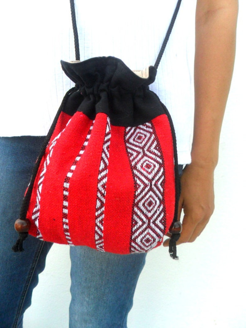 May include: A red and black drawstring bag with a geometric pattern. The bag is made of woven fabric and has a black drawstring closure. The bag is being worn by a person.