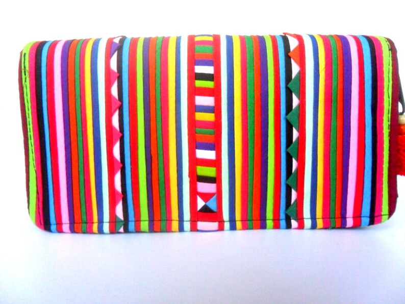 Puede incluir: Un bolso de mano de rayas coloridas con cierre de cremallera. El bolso est&aacute; hecho de un material suave y texturizado y presenta una variedad de colores brillantes, incluyendo rojo, naranja, amarillo, verde, azul, morado y rosa.