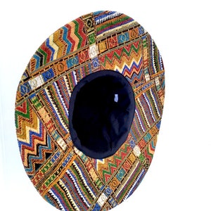 Puede incluir: Un sombrero redondo y plano con un patr&oacute;n geom&eacute;trico colorido. El sombrero est&aacute; hecho de tela y tiene un forro negro.