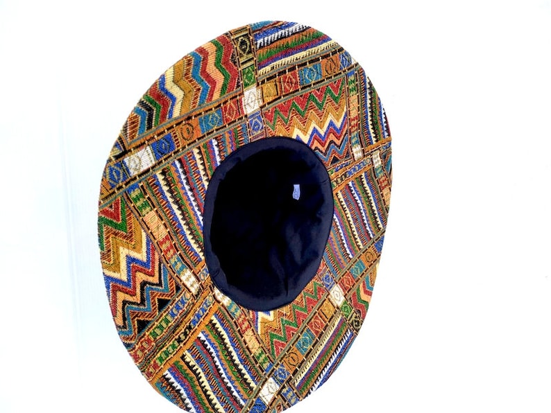 Puede incluir: Un sombrero redondo y plano con un patr&oacute;n geom&eacute;trico colorido. El sombrero est&aacute; hecho de tela y tiene un forro negro.